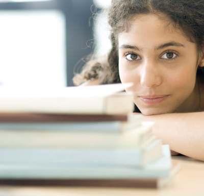 Young woman looking over stack of books at camera